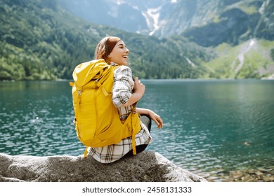 Happy tourist woman  enjoys the view of the mountain lake in sunny weather. Scenery of the majestic mountains. Active lifestyle. - Powered by Shutterstock