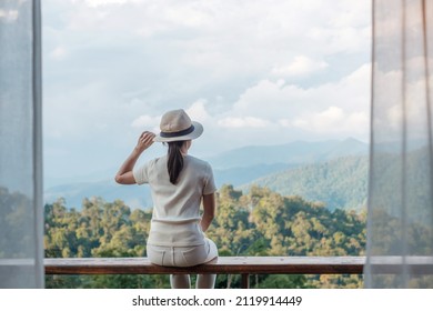 Happy tourist woman relaxing and looking mountain view at countryside home or homestay in the morning. Vacation, blogger, SoloTravel, journey, trip and relaxing concept