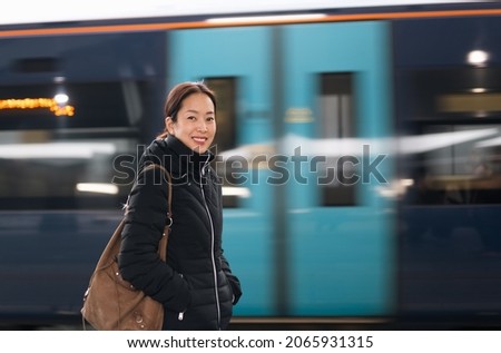 Happy tourist woman standing on the platform with blurred moving train on background