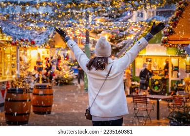 A happy tourist woman stands on a christmas market in Copenhagen, Denmark, with snow and illuminated decorations during winter time