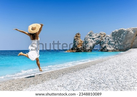 A happy tourist woman in a white summer dress enjoys the beautiful beach of Lalaria, Skiathos island, Greece