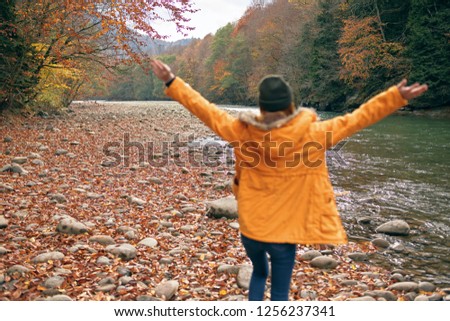 Happy tourist in a yellow jacket with raised arms near a mountain river in the forest                        