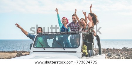 Happy tourists friends doing excursion in desert on convertible jeep car - Young people having fun traveling together - Friendship, youth lifestyle and vacation concept - Focus on guys with hands up