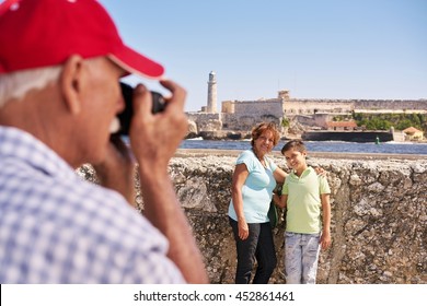 Happy Tourists On Holidays. Hispanic People Traveling In Havana, Cuba. Grandfather, Grandmother And Grandchild During Summer Travel, With Senior Man Taking Photos With Camera