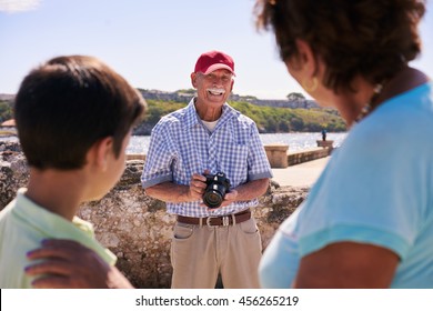 Happy Tourists On Holidays. Hispanic People Traveling In Havana, Cuba. Grandfather, Grandmother And Grandchild During Summer Travel, With Senior Man Taking Photos With Camera