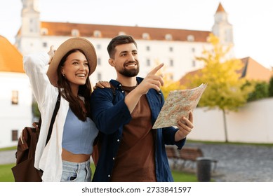 Happy tourists smiling, using map while looking around the city on sunny day, planning route to landmarks, free space