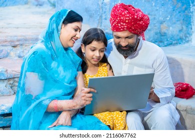 Happy Traditional Indian Family Using Laptop, Girl Child With Her Parents, Man Wearing Red Turban And Woman Wearing Sari Using Computer, Online Education. Skill India Concept. 