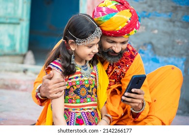 Happy Traidtional Indian Father And Daughter Wearing Colorful Outfits And Using Smart Phone, Smiling Beard Man With Little Girl Watching Video, Social Media Internet, Android Smart Mobile Phone.