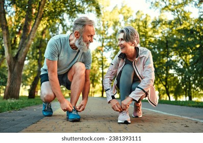 Happy training together. Active spouses on retirement taking break after jogging and squatting for tying laces on sneakers. Happy husband and wife looking at each other and smiling. - Powered by Shutterstock