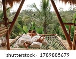 Happy travel couple on hammock balcony of bamboo tree house with jungle nature view. vacation in beaitiful hidden place, honeymoon on Bali island