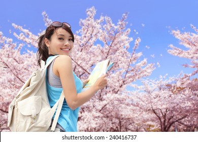 Happy travel woman look map and smile with sakura cherry blossoms tree on vacation while spring, asian