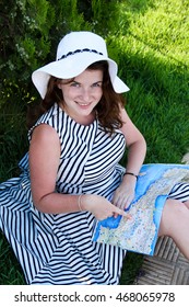 Happy travel woman look map sitting on grass in striped dress