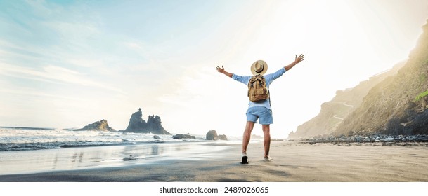 Happy traveler with hands up standing at the beach - Delightful man enjoying success and freedom outdoors - Wanderlust, wellbeing, travel and summertime holidays concept - Powered by Shutterstock