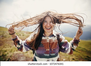 happy traveler hipster girl with windy hair and smiling, standing on top of sunny mountains. space for text. stylish woman waving hair. atmospheric moment. travel and wanderlust
