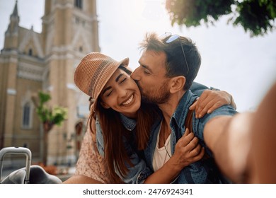Happy traveler kissing his girlfriend while taking selfie in the city.  - Powered by Shutterstock