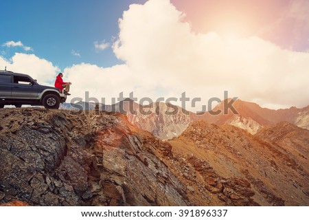 Happy Traveler man sitting on his car on mountains top. 4x4 travel trekking 