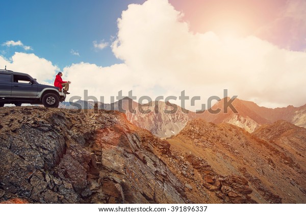 Happy Traveler man sitting on his car on\
mountains top. 4x4 travel trekking\
