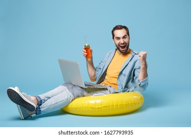 Happy Traveler Tourist Man In Summer Clothes Isolated On Blue Background. Passenger Travel On Weekend. Air Flight Journey. Sit In Inflatable Ring Work On Laptop, Hold Beer Bottle Doing Winner Gesture