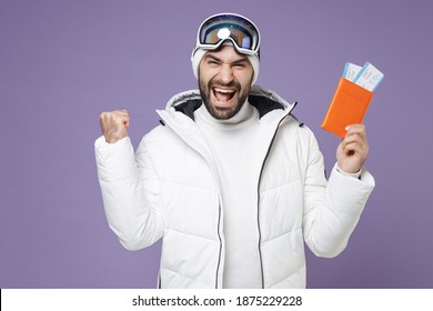 Happy Traveler Tourist Skier Man In Warm White Jacket Ski Goggles Mask Hold Passport Tickets Doing Winner Gesture Spend Weekend Winter In Mountains Isolated On Purple Background. People Hobby Concept