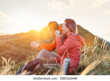 Happy traveler young couple resting in the mountains and drinking tea from thermos at sunset in spring or summer season. - Powered by Shutterstock