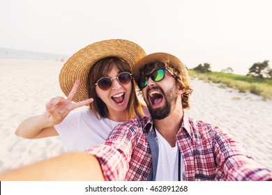 Happy  traveling  couple in love  taking a selfie on phone  at the beach on a sunny summer day.  Pretty girl and her handsome boyfriend with beard    having fun, crazy emotional faces , laughing.  - Powered by Shutterstock