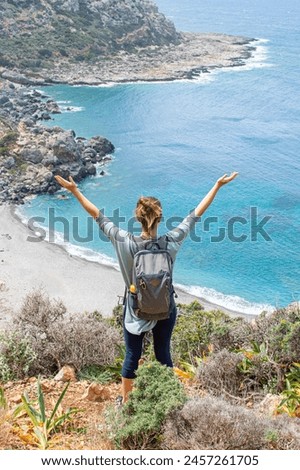 Happy traveller, woman hiking in Crete island, amazing view of the dark beach, on the walk in Greece. Wild beach. Enjoying the sea view. 