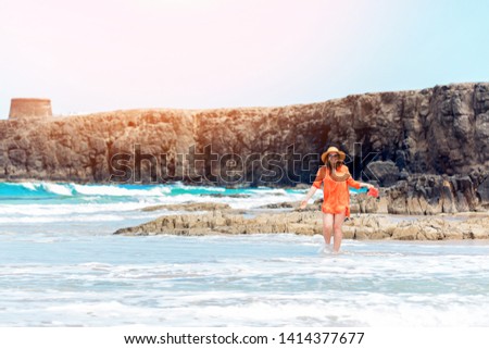 Happy traveller woman in orange dress enjoys her tropical beach vacation