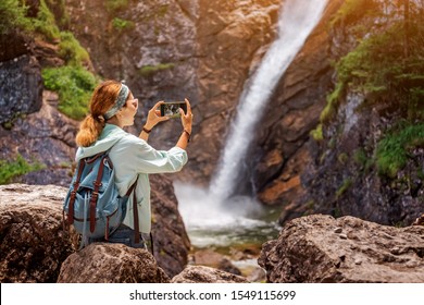 Happy traveller woman taking photo of majestic waterfall in the jungle. Hiking and sightseeing concept - Powered by Shutterstock