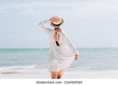 Happy traveller woman in white dress and hat enjoys her tropical beach vacation - Shutterstock ID 2164369265