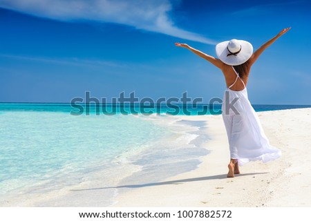 Happy traveller woman in white dress enjoys her tropical beach vacation
