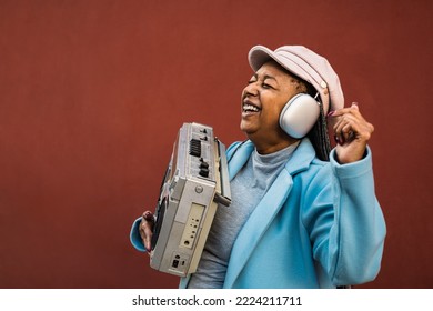 Happy trendy senior African woman having fun dancing while listening music with headphones and vintage boombox stereo - Powered by Shutterstock