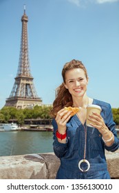 Happy Trendy Solo Traveller Woman In Blue Jeans Overall With Cup Of Coffee And Croissant In Paris, France.