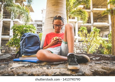 Happy Trendy Student Taking A Break Of Study And Eat A Fruit Healthy Snack After School Under Trees. Young Boy Doing Breakfast Meal In Nature Youth Lifestyle Millennials Generation Health Food Concept