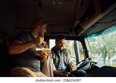 Happy Truck Driver And His Colleague Eating During Lunch Break In A Cabin.