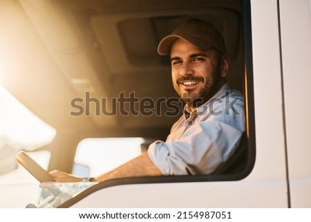 Happy truck driver sitting in vehicle cabin and looking at camera.