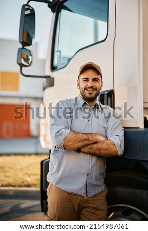 Happy truck driver standing with arms crossed in front of his truck and looking at camera.
