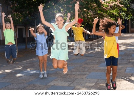 Happy tween girl having fun outdoors with friends of different nationalities, jumping on city street in summer day..