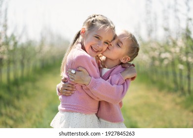 Happy twin sisters hug against the background of a green blooming Apple orchard. One sister kisses the other on the cheek. - Powered by Shutterstock