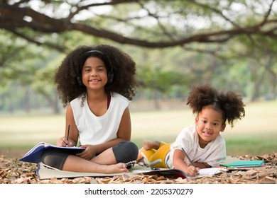 Happy two African American child girl sitting and writing on a book outdoors in the park. Kids girl learning outside at the school - Powered by Shutterstock