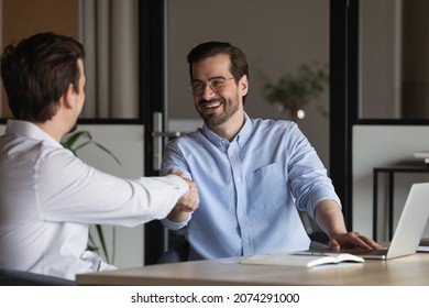 Happy two diverse colleagues shaking hands, celebrating making agreement at office meeting. Smiling businessmen establishing partnership at workplace, successful cooperation collaboration concept. - Shutterstock ID 2074291000