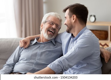 Happy Two Generations Male Family Laugh Enjoy Talking Bonding Embracing Sit On Sofa At Home, Old Senior Father And Young Adult Grown Son Relaxing Having Fun Hugging Chatting On Couch On Fathers Day