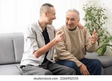 Happy two generations male family old senior mature father and smiling young adult grown son enjoying talking chatting bonding relaxing having friendly positive conversation sit on sofa at home. - Powered by Shutterstock