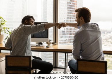 Happy two male colleagues bumping fists, greeting each other or showing team union. Joyful young business partners celebrating shared success, sitting at table in modern workplace. - Powered by Shutterstock