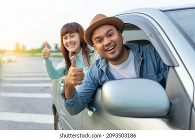 Happy Two Young Friends Driver Smiling While Sitting In A Car. Asian Man And Woman Showing Thump Up And Chreeful Through Window. Young Couple Wear Hats Driving Car To Travel On Holiday Vacation Time.