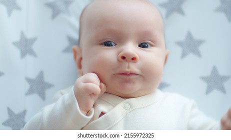 Happy Two-month-old Baby In Blue Clothes Looks Into Camera. Active And Cheerful Newborn Boy Lies On The Sofa And Moves His Arms. Funny And Cute Chubby Male Baby. Beautiful Infant.