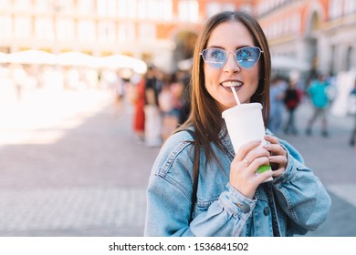 Happy Urban Woman With Blue Sunglasses Enjoying Her Morning Drinking A Soda In Styrofoam Cup With Straw. Pretty Girl In The Street. Take Away Beverages Concept.