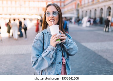 Happy Urban Woman With Blue Sunglasses Enjoying Her Morning Drinking A Soda In Styrofoam Cup With Straw. Pretty Girl In The Street. Take Away Beverages Concept.