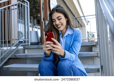 Happy urban woman drinks her takeaway coffee and talk on smartphone. Young woman sits on stairs with tea and holding mobile phone. - Powered by Shutterstock