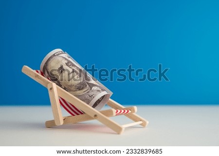 Happy US dollar bill banknote rest on wooden beach chair with blue background copy space in summer beach holiday. Financial freedom through passive income, success wealth from investment concept.