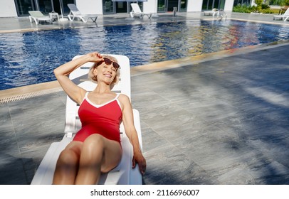 Happy vacation. Senior woman in red swimwear on the sunlounger near the swimming pool.